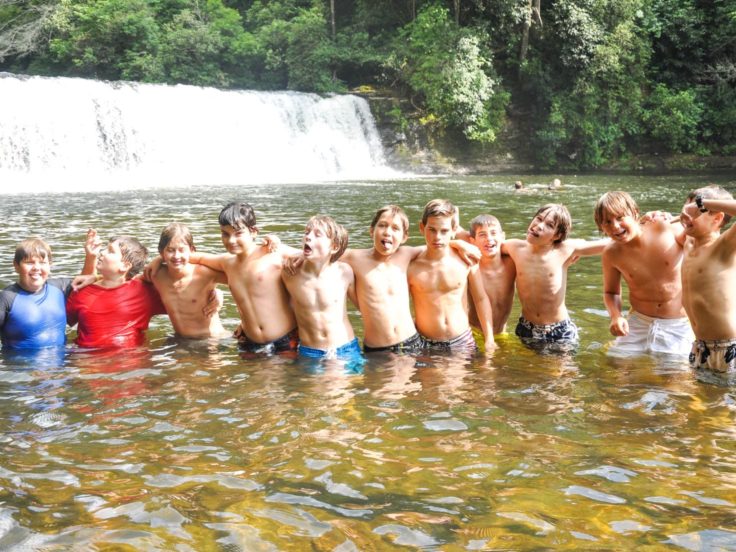 Boys in bathing suits standing in river by waterfall on the Rock Climbing & Canoeing Pioneer Expedition