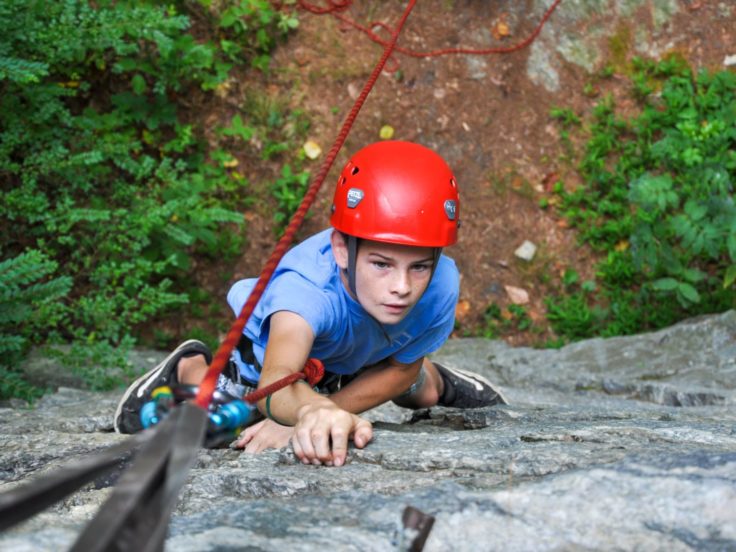Young male climber reaching for hold on a rock wall on the Rock Climbing & Canoeing Pioneer Expedition