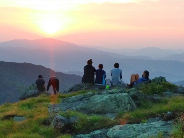 Campers sitting on a mountain, looking out at the sunset